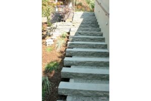 Grey stone steps leading up to backyard with handrail and Japanese maple nearby.